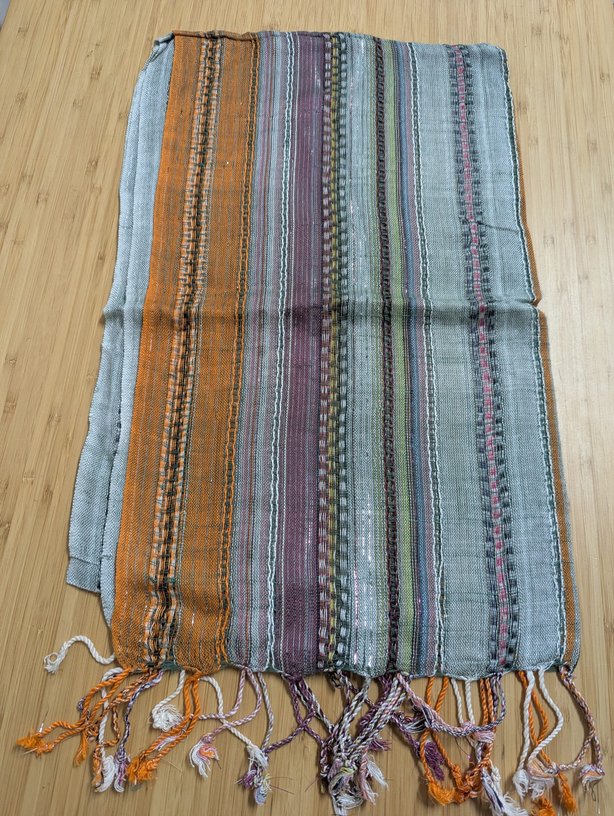 A softly textured woven scarf featuring vertical stripes in shades of light blue, copper orange, and mauve, finished with short fringe tassels at both ends.