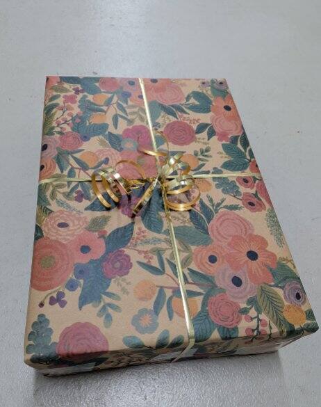 Gift box wrapped in floral paper with a gold ribbon on a light gray background