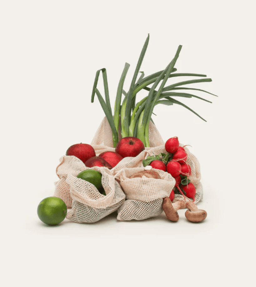 Seed & Sprout mesh organic cotton produce bags filled with fresh apples, limes, radishes, mushrooms, and spring onions.