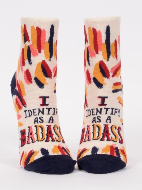 A pair of cream Blue Q women's ankle socks featuring abstract brushstrokes and text reading "I IDENTIFY AS A BADASS."