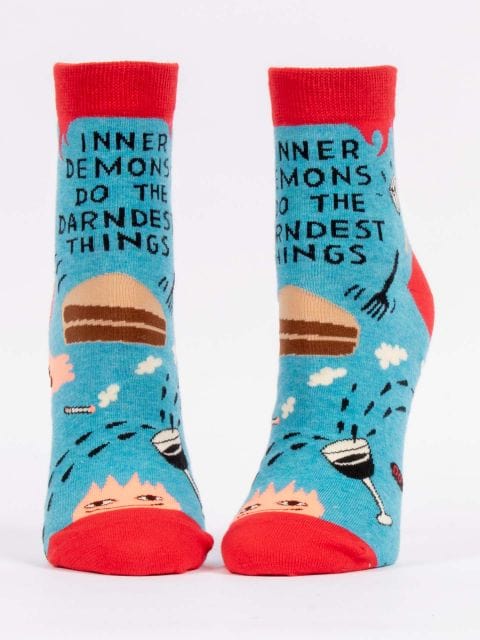 A pair of Blue Q ankle socks with a blue and red design featuring text and cartoonish figures. The socks say 'INNER DEMONS DO THE DARNEST THINGS'.