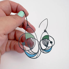 Hand holding a pair of DENZ Art School Drop Out Earrings in Cool geometric with a white background