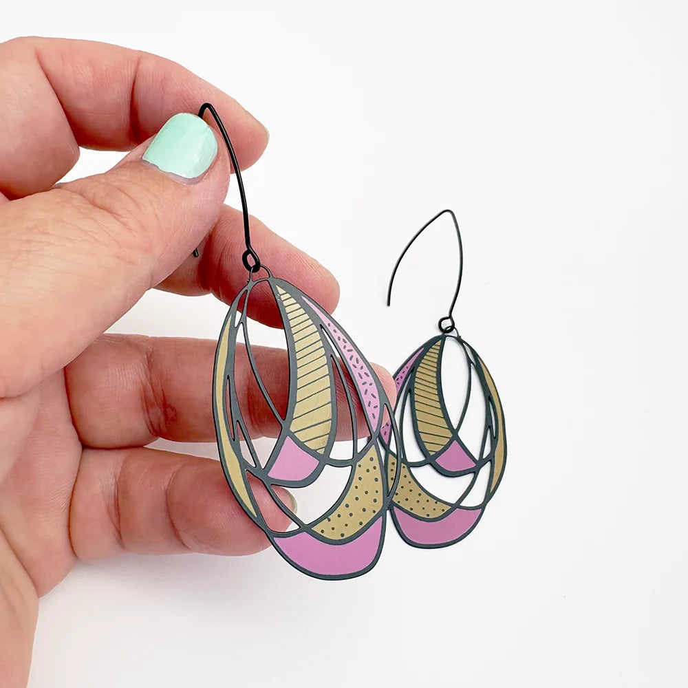 Hand holding a pair of DENZ Art School Drop Out earrings against a white background