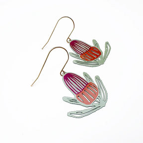 A pair of DENZ banksia flower dangling earrings with fishhook wires and stylized seed or pod shapes in sage, orange, and wine, set outline on a white background.