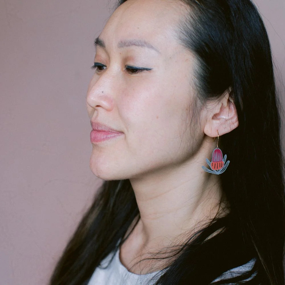 Woman wearing a DENZ  colorful banksia floral earring against a plain background
