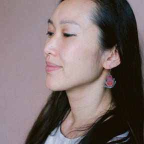 Woman wearing a DENZ  colorful banksia floral earring against a plain background