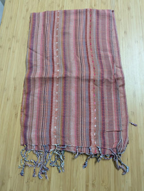 Flat-lay photograph of a woven scarf featuring vertical stripes in shades of dusty rose, mauve, and plum, displayed flat on a smooth wooden background with a crisp, ironed finish and detailed twisted fringe tassels along the bottom edge.