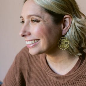 Woman wearing DENZ How's The Serenity earrings in mustard with text, smiling against a neutral background
