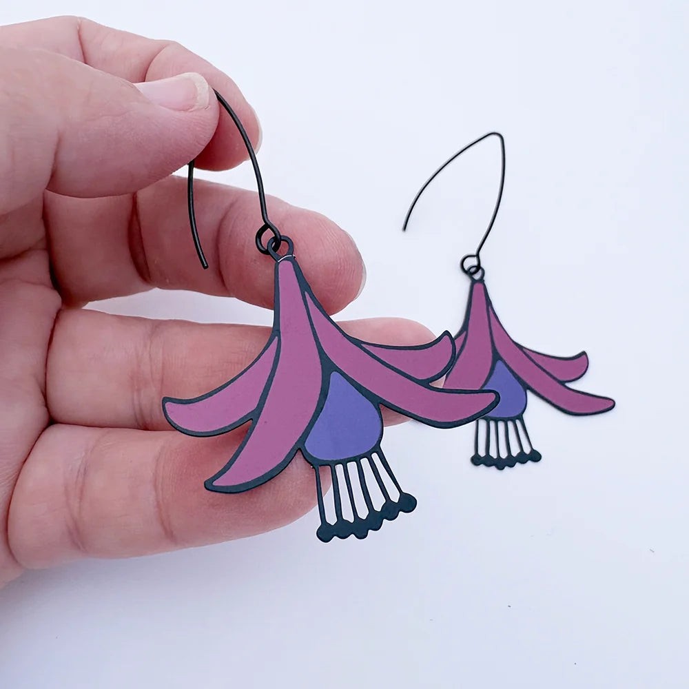 Hand holding a pair of DENZ Fuchsia Flower Earrings with a white background