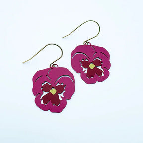 A pair of DENZ dangling earrings with magenta-pink flower-shaped cutouts and gold-tone fishhook wires, shown on a plain white background.