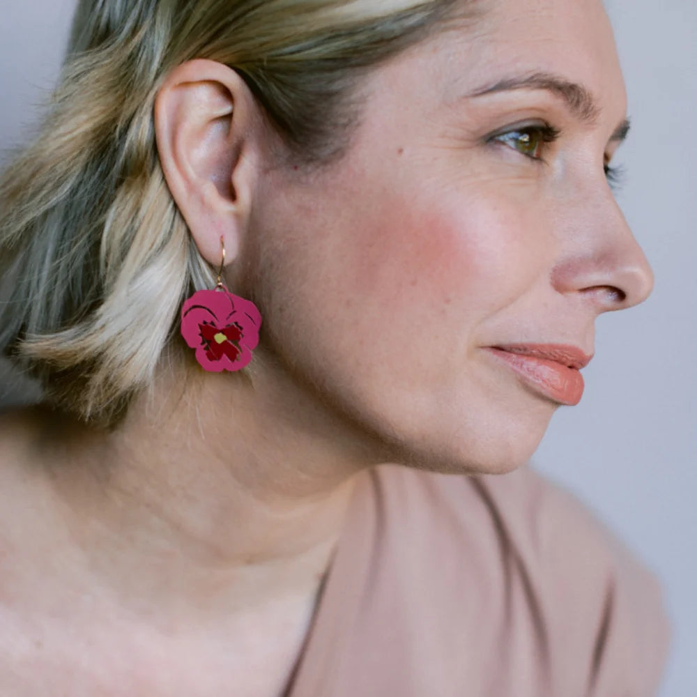 A close-up side profile of a woman wearing a DENZ Pansy Flower and gold hook, against a soft light gray background.
