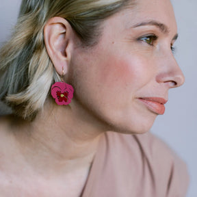 A close-up side profile of a woman wearing a DENZ Pansy Flower and gold hook, against a soft light gray background.