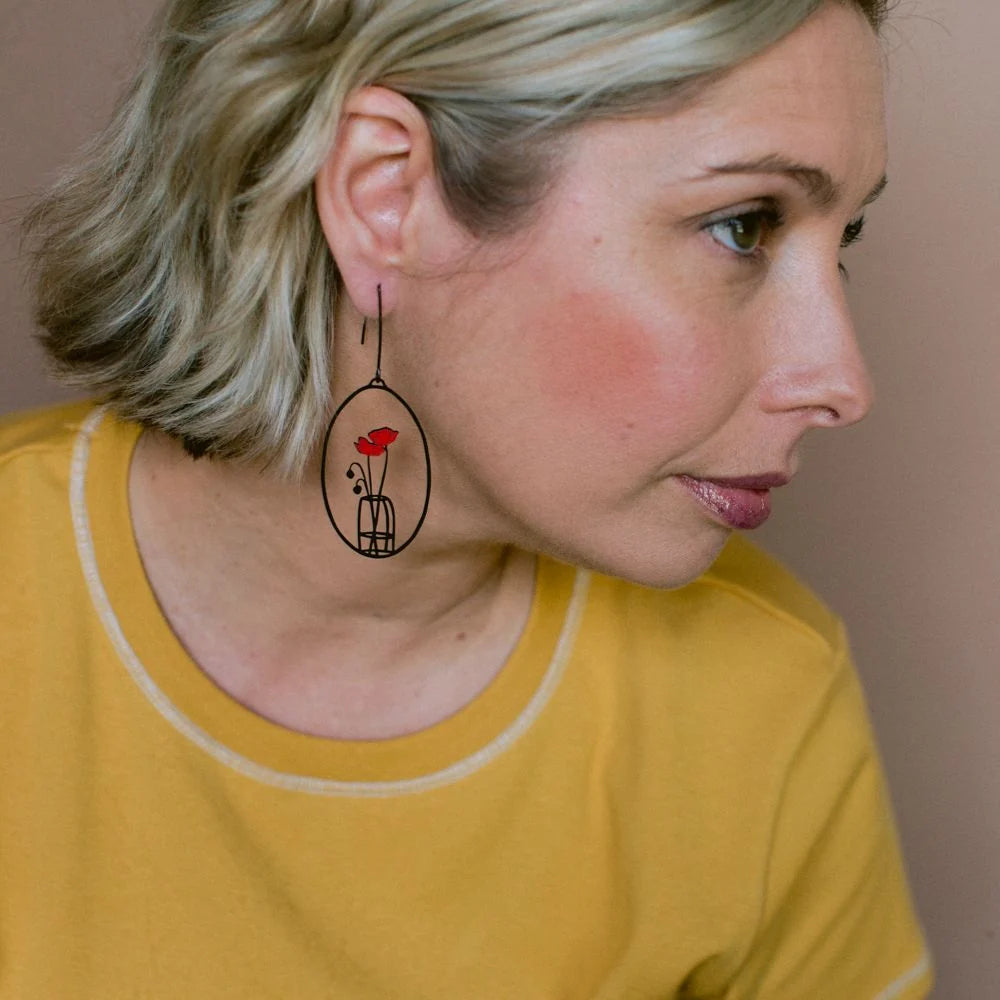Woman wearing a unique DENZ Poppy Vase earring with a red flower design on a plain background