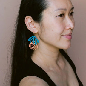 Woman wearing colorful DENZ Protea Flower dangle earrings against a neutral background