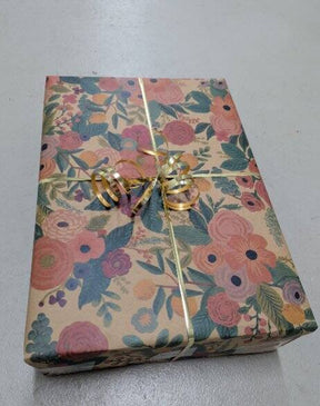 Gift box wrapped in floral paper with a gold ribbon on a light gray background