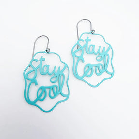 A pair of DENZ mint blue laser-cut metal dangle earrings with the phrase 'Stay Cool' in cursive script.