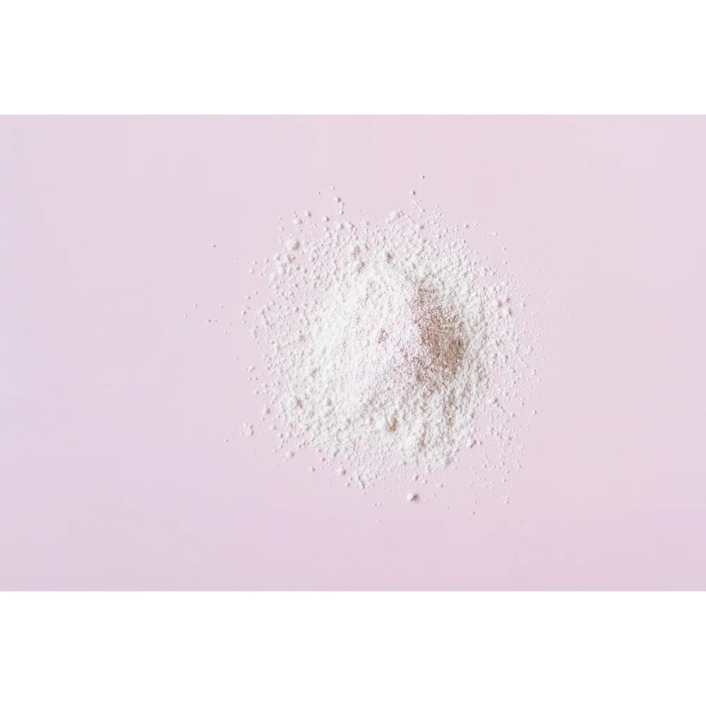 A small pile of white powder from Summer Salt Body Mini White Clay Masque 40g centered on a soft pink background.