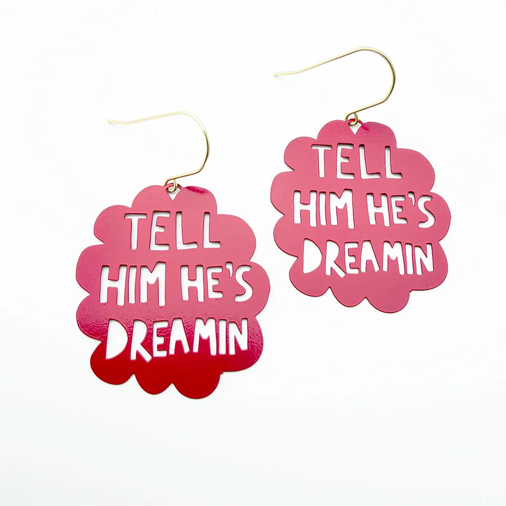 A pair of DENZ pink cloud-shaped dangle earrings with gold fishhook wires. The front of each earring features a scalloped red gradient overlay containing the white text 'TELL HIM HE'S DREAMIN'.