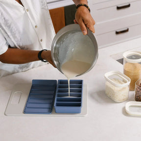 Seed & Sprout blue 6-portion silicone freezer tray being filled with batter poured from a stainless steel mixing bowl on a modern kitchen counter.
