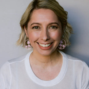 Front-facing portrait of a smiling woman wearing DENZ Flannel Flower Earrings in Pinks & White 