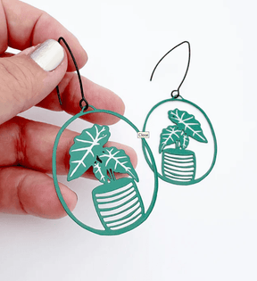 DENZ Midi Alocasia plant earrings in Green/White, held by hand