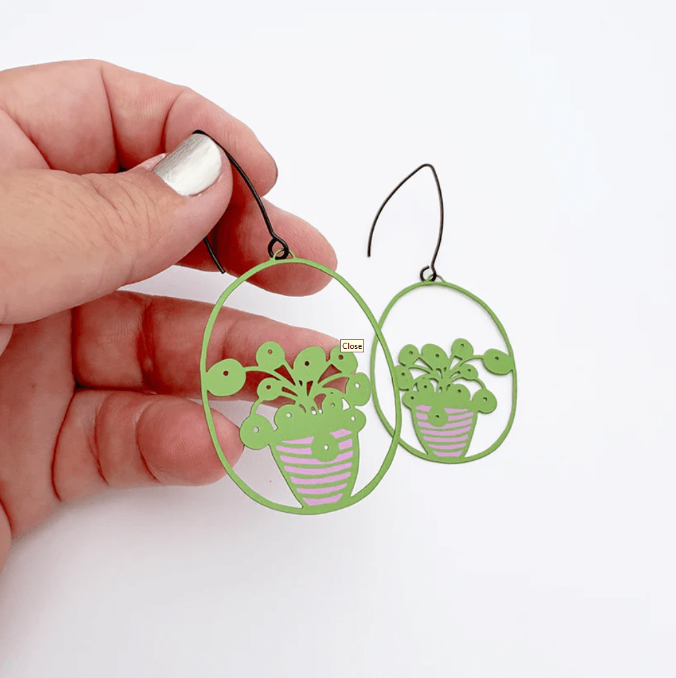 DENZ Midi Pilea plant earrings in Bright Green/Pink, held by hand