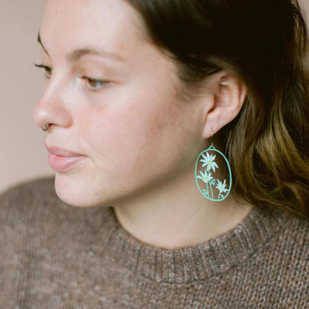 A close-up side profile of a woman wearingDENZ Flannel Flower earring, paired with a brown knit sweater against a soft beige background.