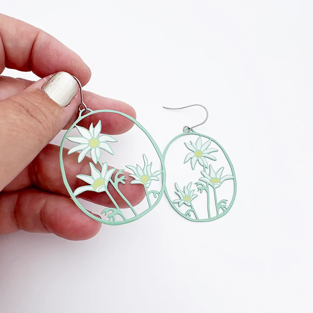 Hand holding a pair of DENZ Flannel Flower earrings with a white background