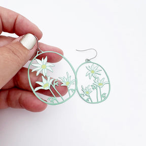 Hand holding a pair of DENZ Flannel Flower earrings with a white background