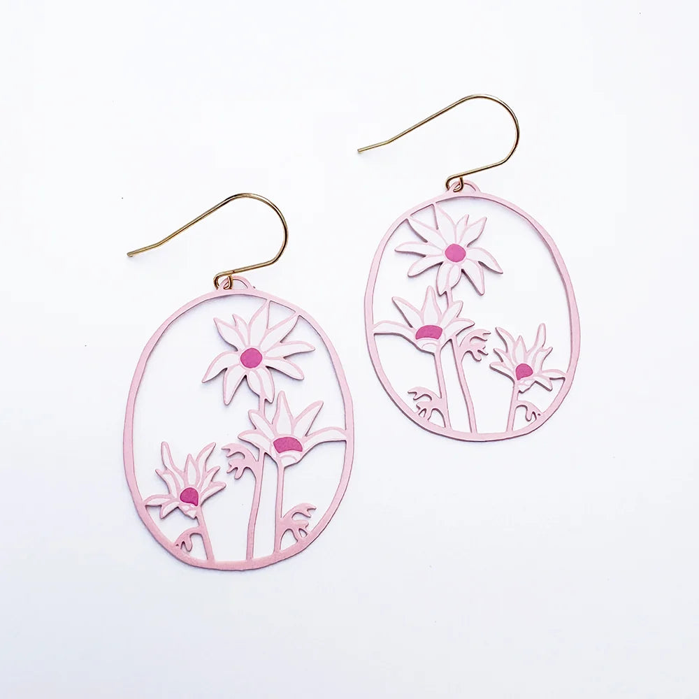 A pair of DENZ oval drop earrings with a light pink laser-cut floral design and gold-tone fishhook ear wires, displayed on a clean white background.