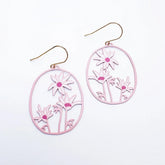 A pair of DENZ oval drop earrings with a light pink laser-cut floral design and gold-tone fishhook ear wires, displayed on a clean white background.
