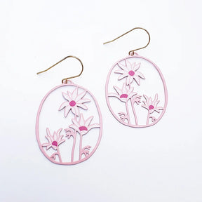 A pair of DENZ oval drop earrings with a light pink laser-cut floral design and gold-tone fishhook ear wires, displayed on a clean white background.