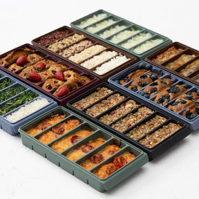 Seed & Sprout compartmented silicone freezer trays in various earthy tones filled with baked berry cakes, muesli slices, rice, and cheesy casseroles.