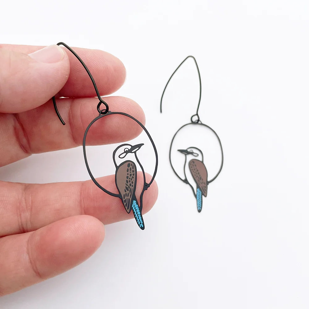 DENZ Kookaburra earrings held by a hand on a white background