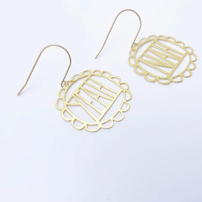 A pair of DENZ gold-toned dangle earrings with scalloped circular cutout frames and a central geometric design, displayed on a clean white background.