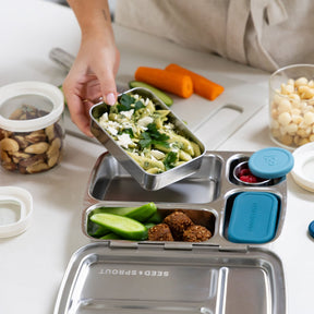 Seed & Sprout stainless steel CrunchBox bento lunch box insea glass being packed with a container of pesto pasta on a kitchen counter.