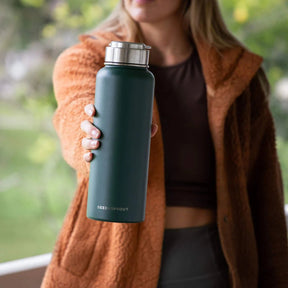 A person holding a Seed & Sprout 1200ml Insulated Stainless Steel Drink Bottle in Moss with a silver cap and embossed brand logo.