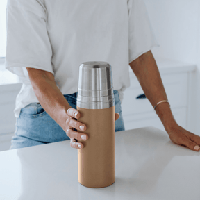 A person holding a Seed & Sprout closed  insulated stainless steel drink flask  in praline on a white kitchen counter.
