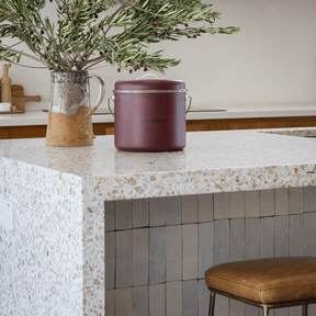 Seed & Sprout mulberry kitchen compost bin displayed on a modern terrazzo countertop next to an earthy ceramic vase filled with leafy branches.