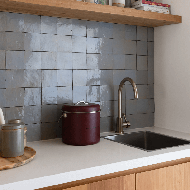 Seed & Sprout mulberry kitchen compost bin placed neatly on a white countertop next to a stainless steel sink and stylish tiled backsplash.