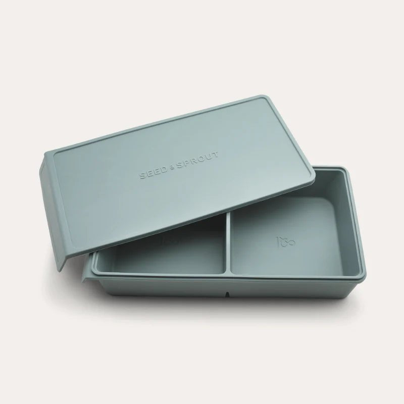 An open Seed & Sprout 2 Portion Silicone Freezer Tray with two partitioned sections and its matching embossed lid resting partially on top.