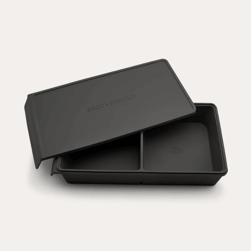 An open Seed & Sprout 2 Portion Silicone Freezer Tray in Liquorice with two partitioned sections and its matching embossed lid resting partially on top.