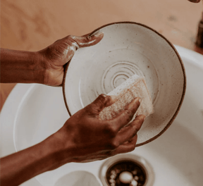 Seed & Sprout compostable cellulose and loofah sponge being used to wash a ceramic bowl in a kitchen sink, highlighting its eco-friendly design and daily functionality.