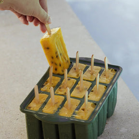 A hand pulling a freshly frozen passionfruit popsicle out of the Seed & Sprout eucalyptus silicone ice pop mold by a pool edge.