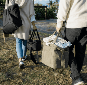 Two people walking outdoors carrying Seed & Sprout insulated cooler bags in olive and charcoal on a sunny day.