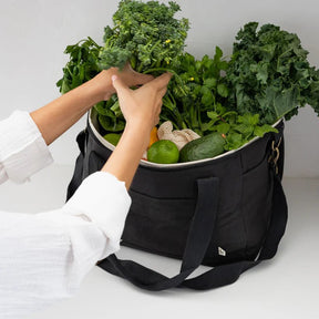 Seed & Sprout charcoal insulated cooler bag being unpacked, filled with fresh leafy greens, broccoli, limes, and avocado.