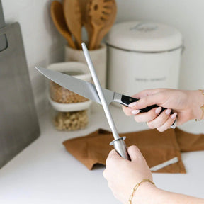 A person sharpening a kitchen knife against a Seed & Sprout Knife Sharpener in a kitchen setting.