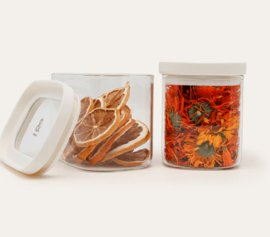 Seed & Sprout Tallow glass storage containers with oatmeal lids, filled with dried orange slices and colorful flower petals.