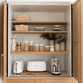 Seed & Sprout Tallow pantry containers and glass storage jars neatly organized on wooden shelves alongside kitchen appliances.