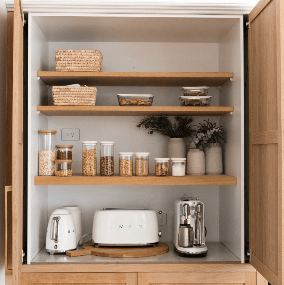 Seed & Sprout Tallow pantry containers and glass storage jars neatly organized on wooden shelves alongside kitchen appliances.